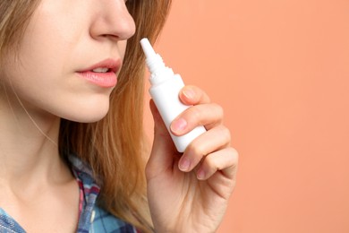 Photo of Sick young woman using nasal spray on coral background, closeup. Space for text