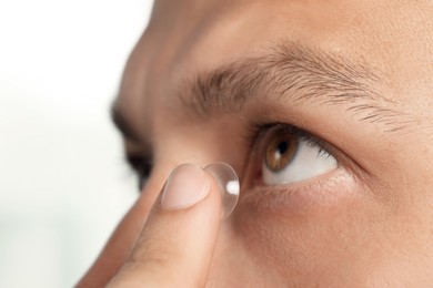 Photo of Man putting contact lens in his eye on white background, closeup