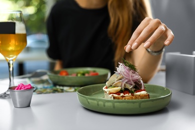 Young woman with tasty fish sandwich in restaurant, closeup