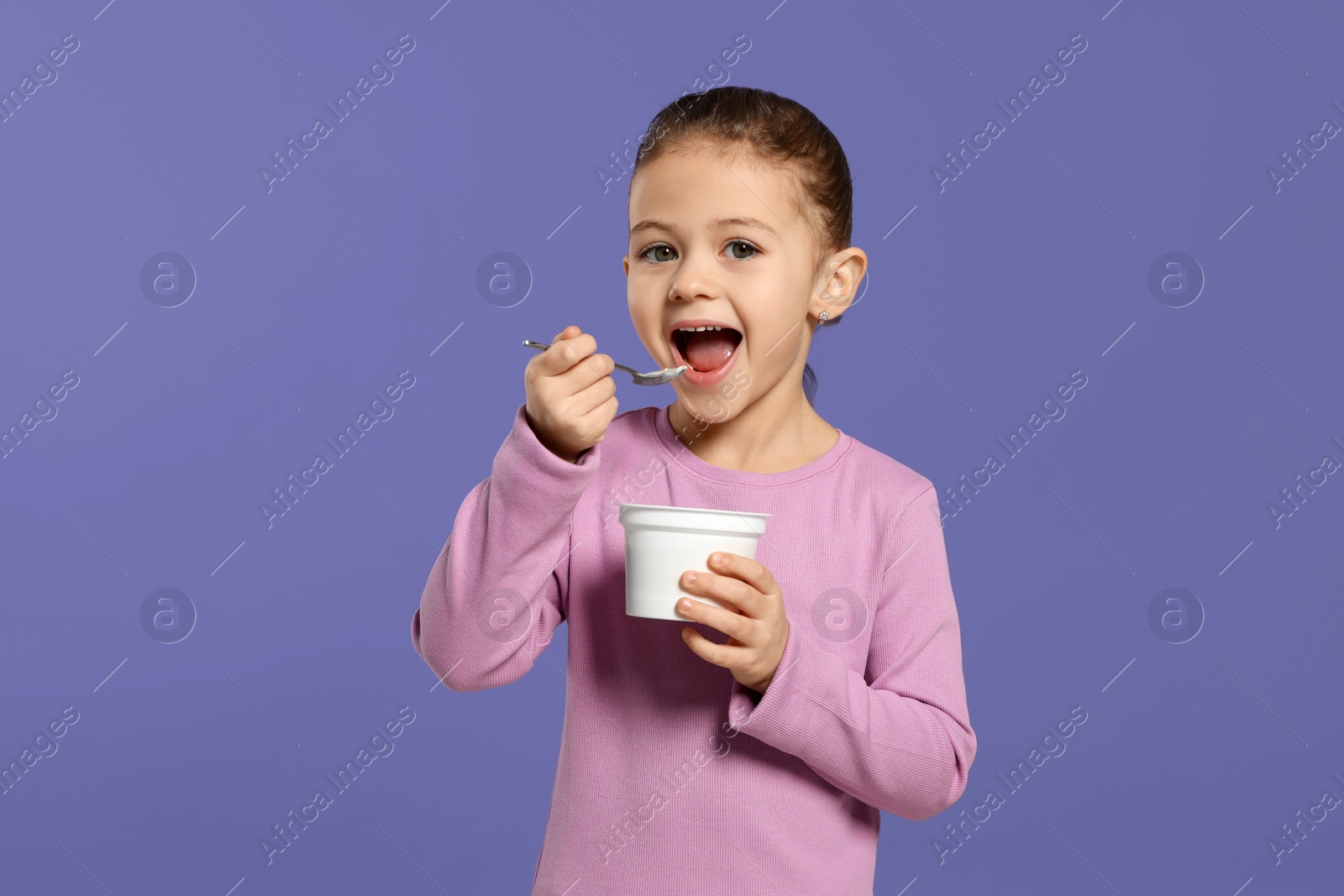 Photo of Girl eating tasty yogurt on violet background