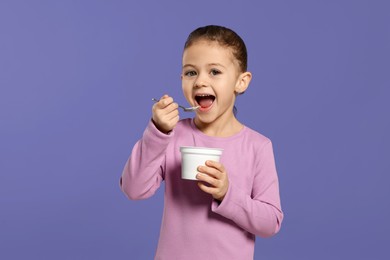 Girl eating tasty yogurt on violet background