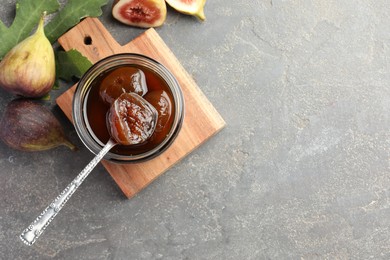 Photo of Jar of tasty sweet jam, fresh figs and green leaf on grey table, flat lay. Space for text