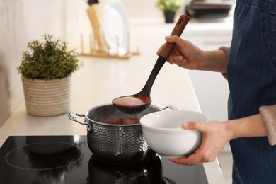 Woman pouring tasty soup into bowl at countertop in kitchen, closeup