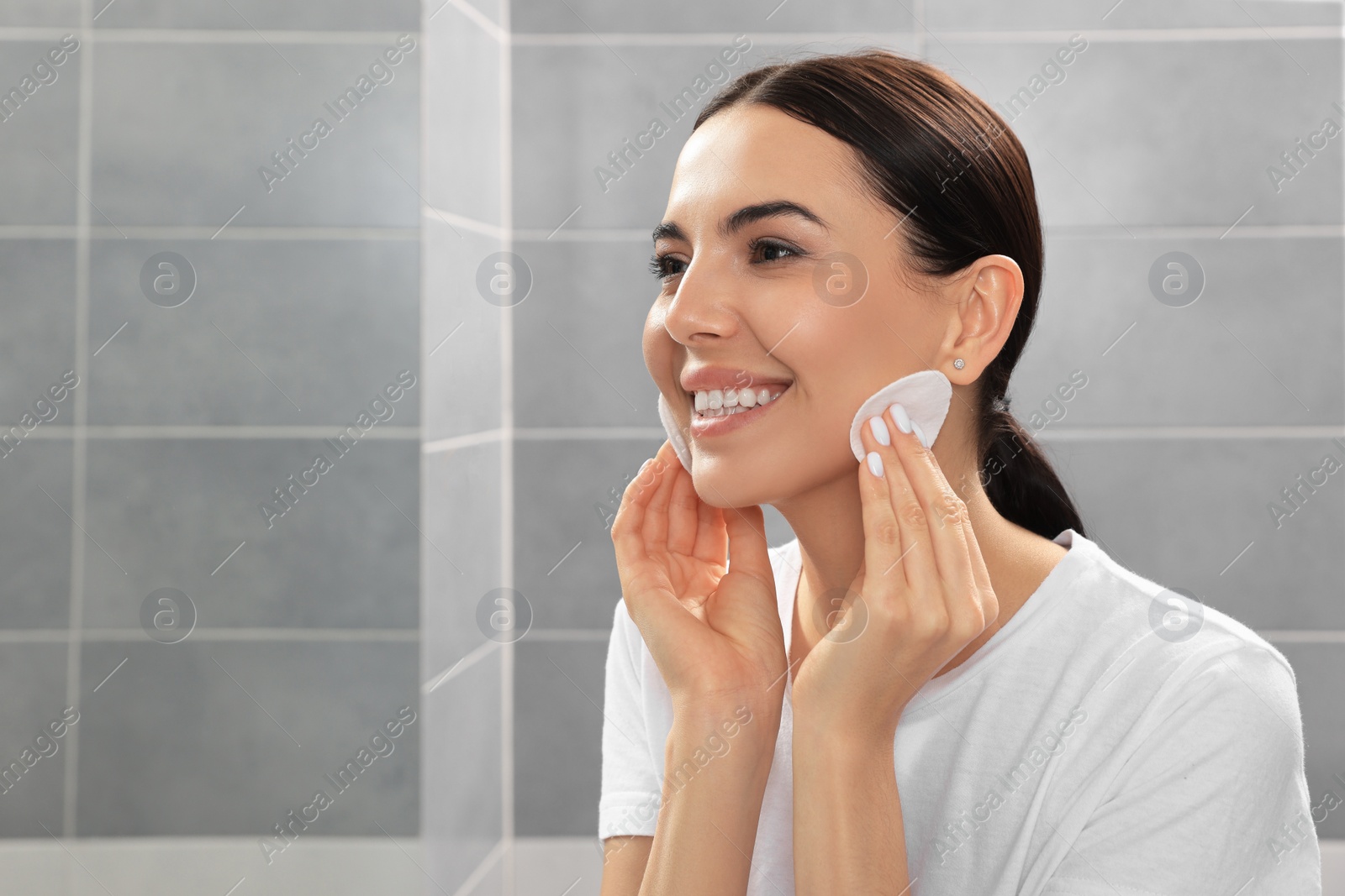 Photo of Young woman using cotton pads with micellar water in bathroom, space for text