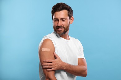 Photo of Man with sticking plaster on arm after vaccination against light blue background