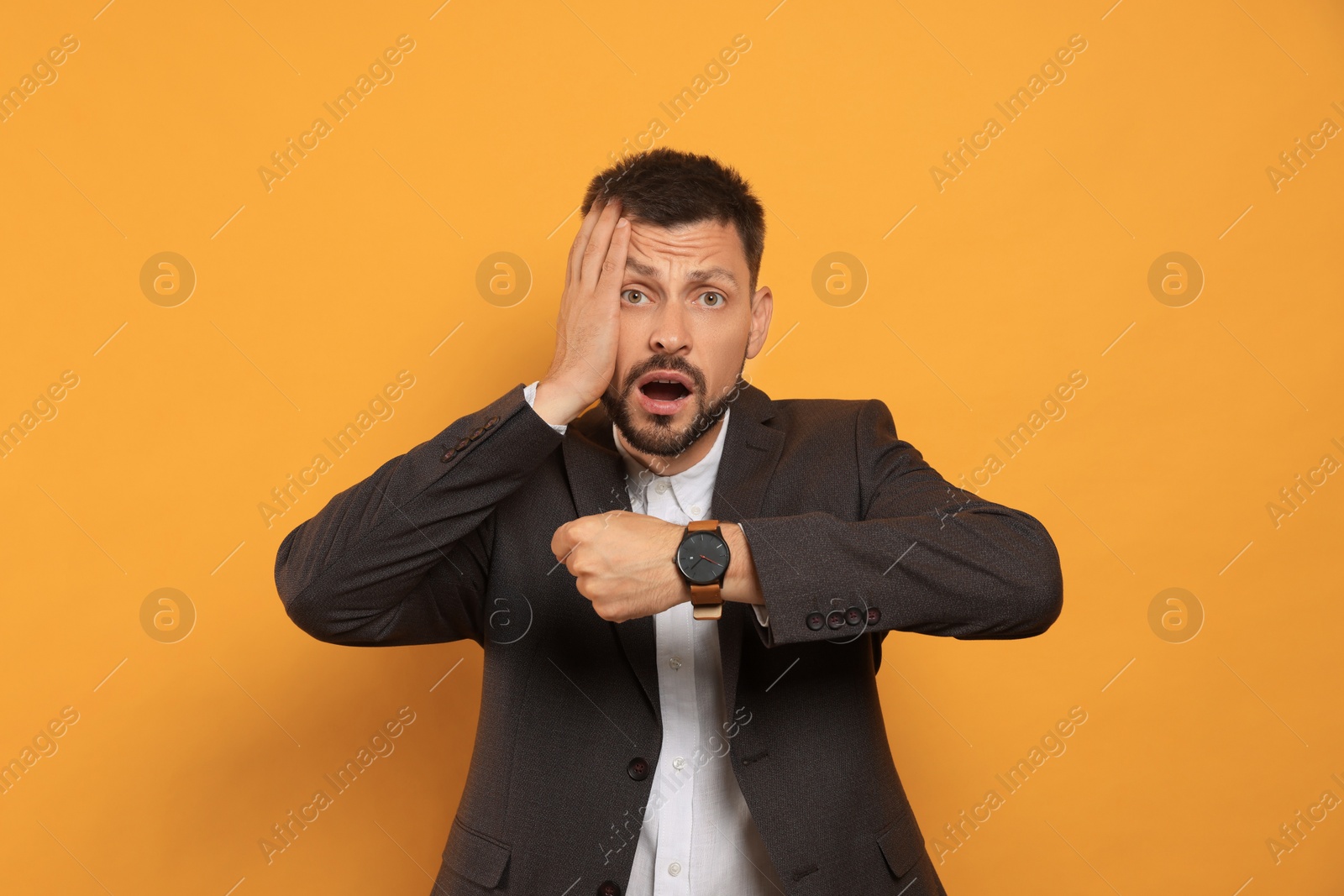 Photo of Emotional man checking time on orange background. Being late concept