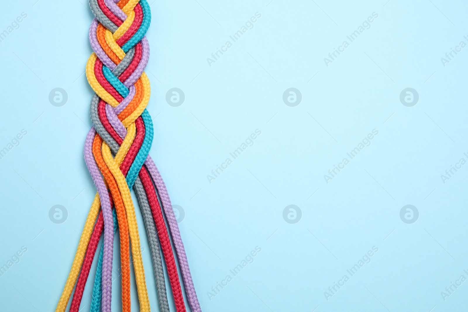 Photo of Top view of braided colorful ropes on light blue background, space for text. Unity concept