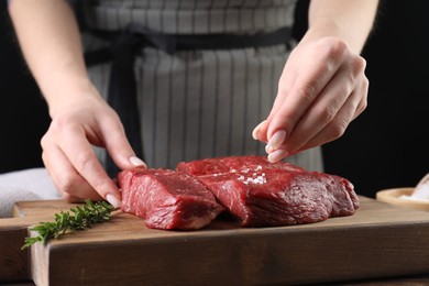 Woman salting fresh raw beef steak at table, closeup