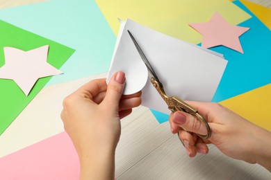 Photo of Woman cutting paper with scissors at white wooden table, closeup