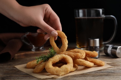 Photo of Woman eating delicious crunchy fried onion ring at wooden table, closeup