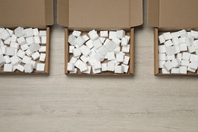 Photo of Open cardboard boxes with pieces of polystyrene foam on wooden floor, flat lay and space for text. Packaging goods