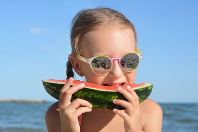 Photo of Cute little girl with sunglasses eating juicy watermelon on beach, closeup
