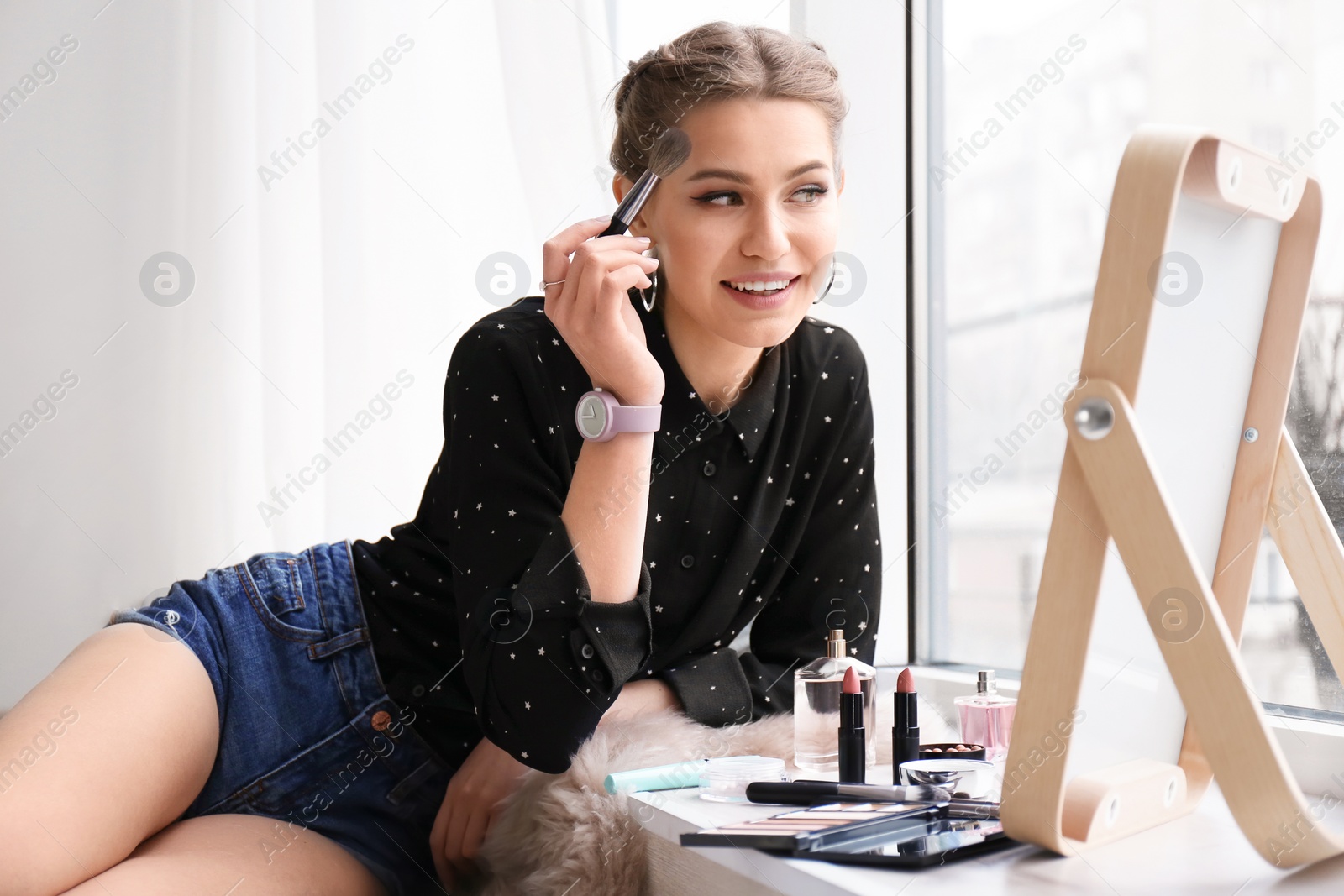 Photo of Portrait of beautiful woman applying makeup near window indoors