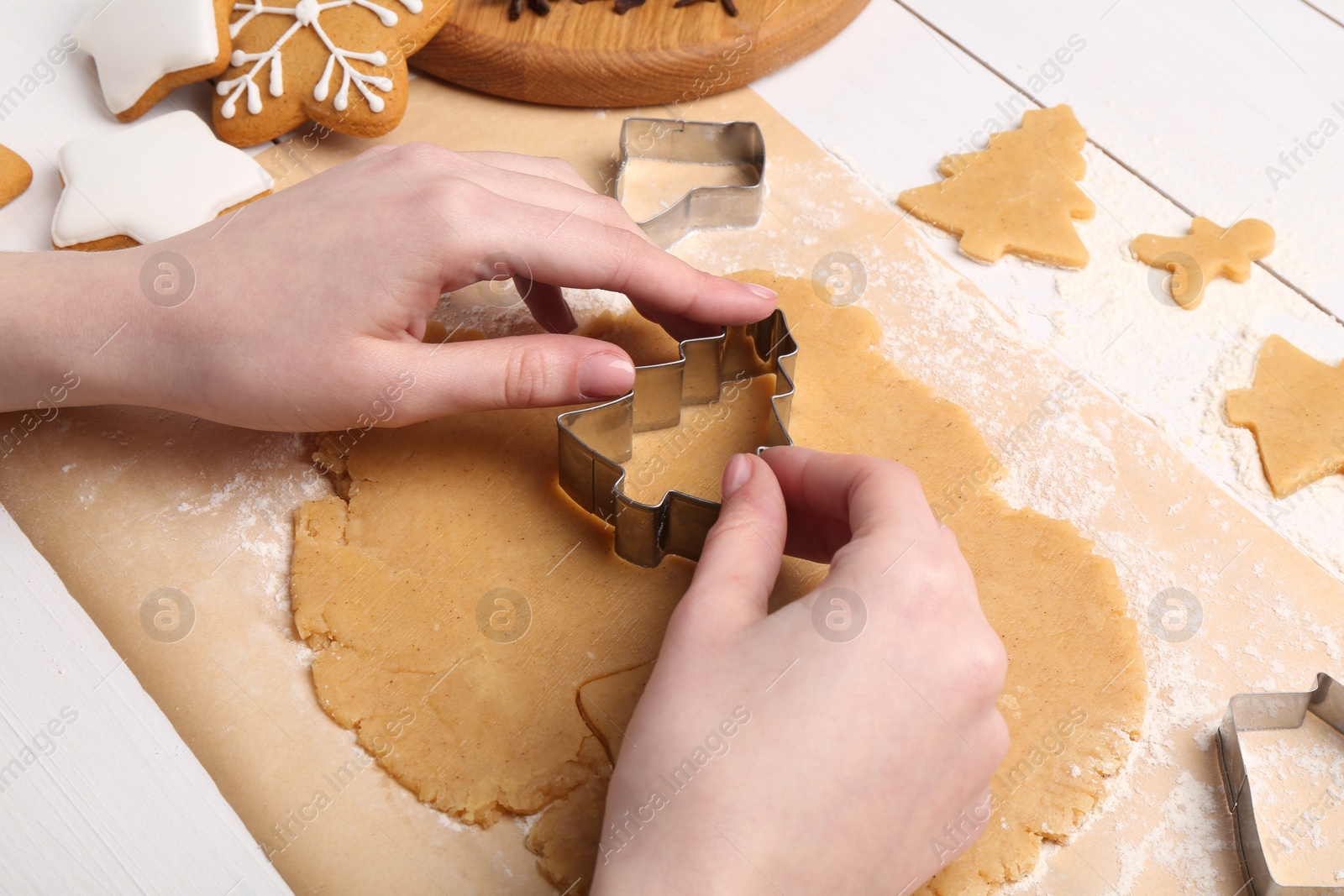 Photo of Woman making Christmas cookies with cutters at white wooden table, closeup