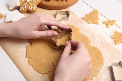 Photo of Woman making Christmas cookies with cutters at white wooden table, closeup