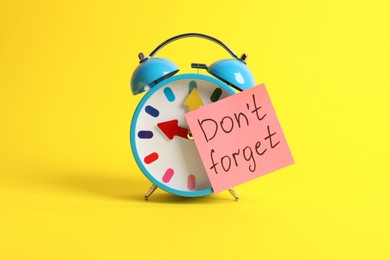 Photo of Alarm clock and reminder note with phrase Don't forget on yellow background