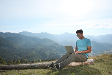 Photo of Man working with laptop in mountains on sunny day