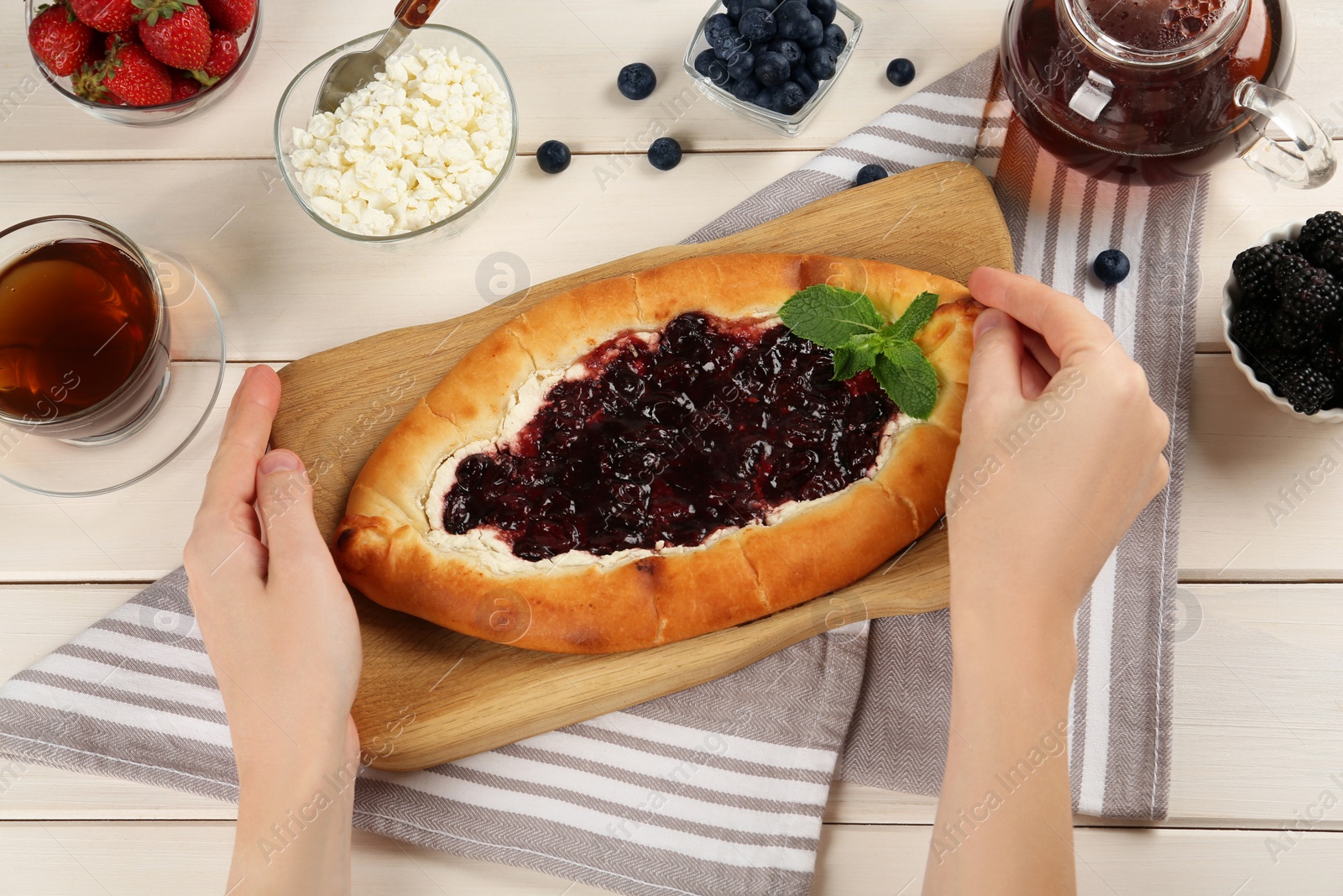 Photo of Woman eating delicious sweet cottage cheese pastry with cherry jam at white wooden table, top view