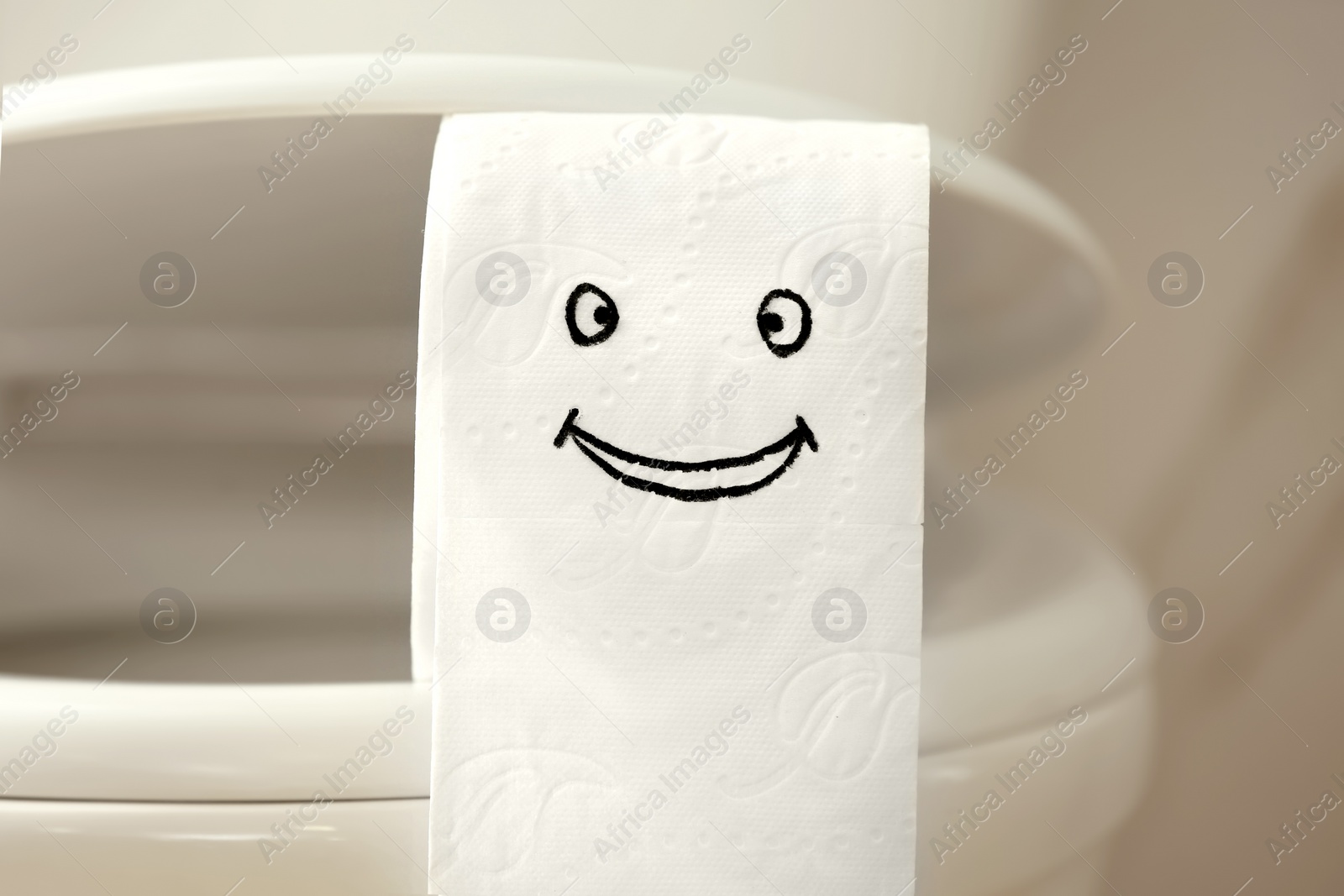 Photo of Roll of paper with funny face on toilet bowl in bathroom, closeup