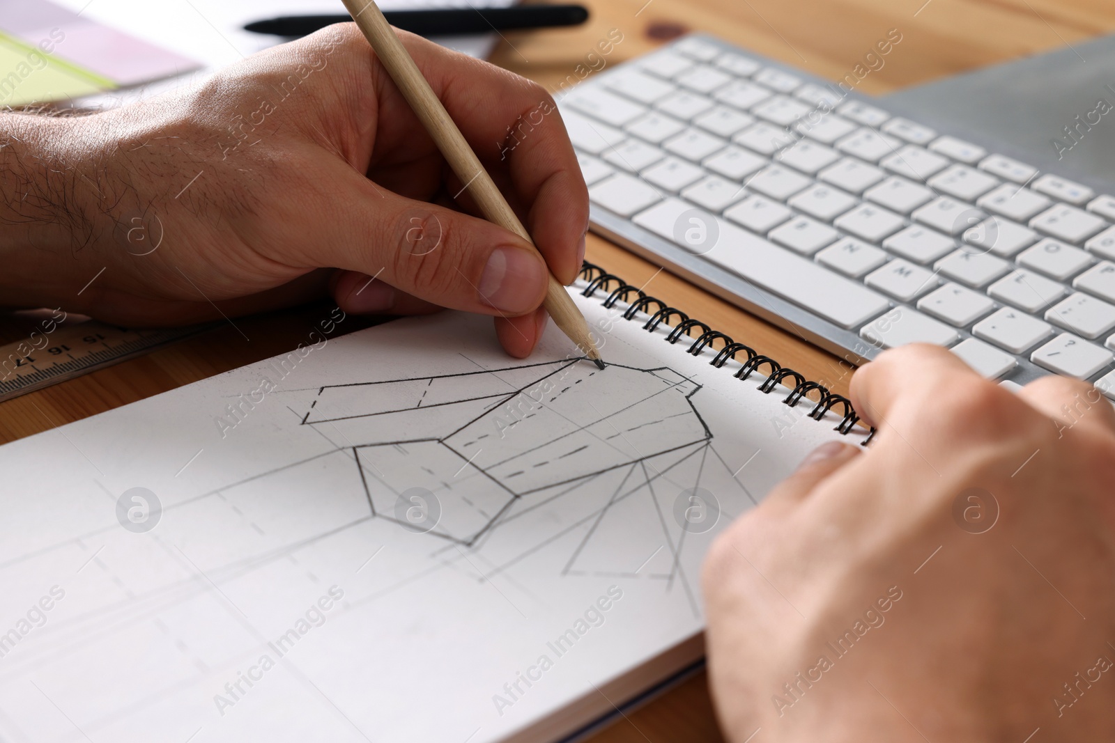 Photo of Man drawing in sketchbook with pencil at wooden table, closeup