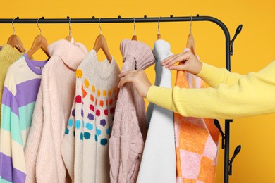 Photo of Woman taking stylish sweater from clothes rack against orange background, closeup