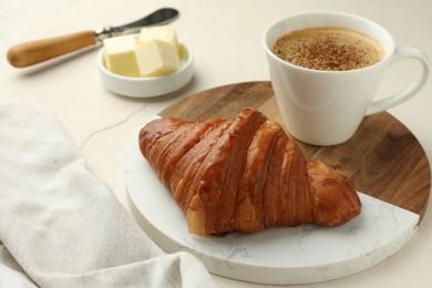 Photo of Tasty croissant served with cup of hot drink on light table, closeup