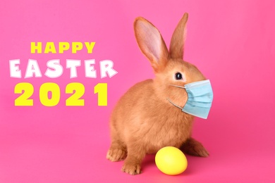 Text Happy Easter 2021 and cute bunny in protective mask on pink background. Holiday during Covid-19 pandemic