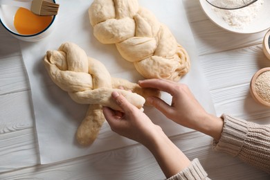 Photo of Woman cooking braided bread at white wooden table in kitchen, top view. Traditional Shabbat challah