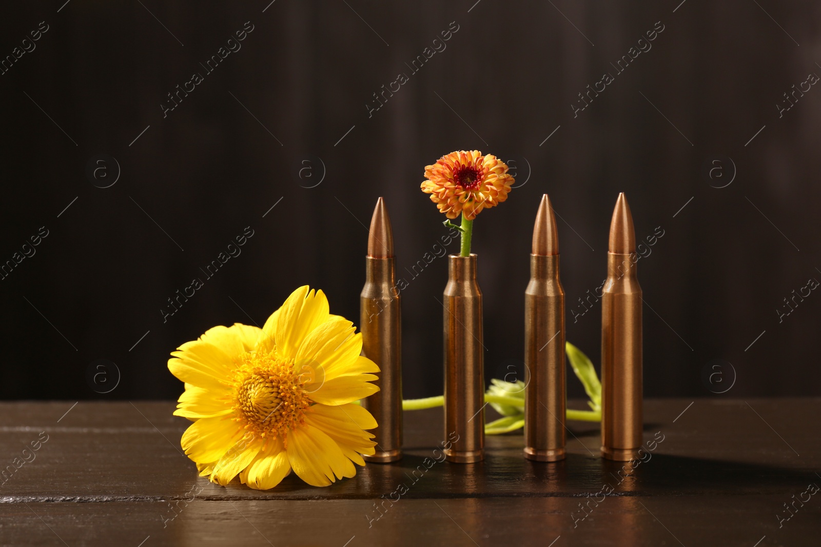 Photo of Bullets and beautiful flowers on wooden table against dark background