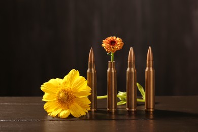 Bullets and beautiful flowers on wooden table against dark background