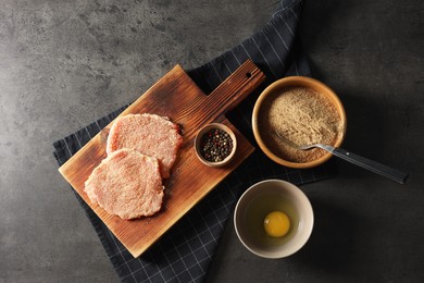Photo of Cooking schnitzel. Raw breaded pork slices and ingredients on grey textured table, flat lay