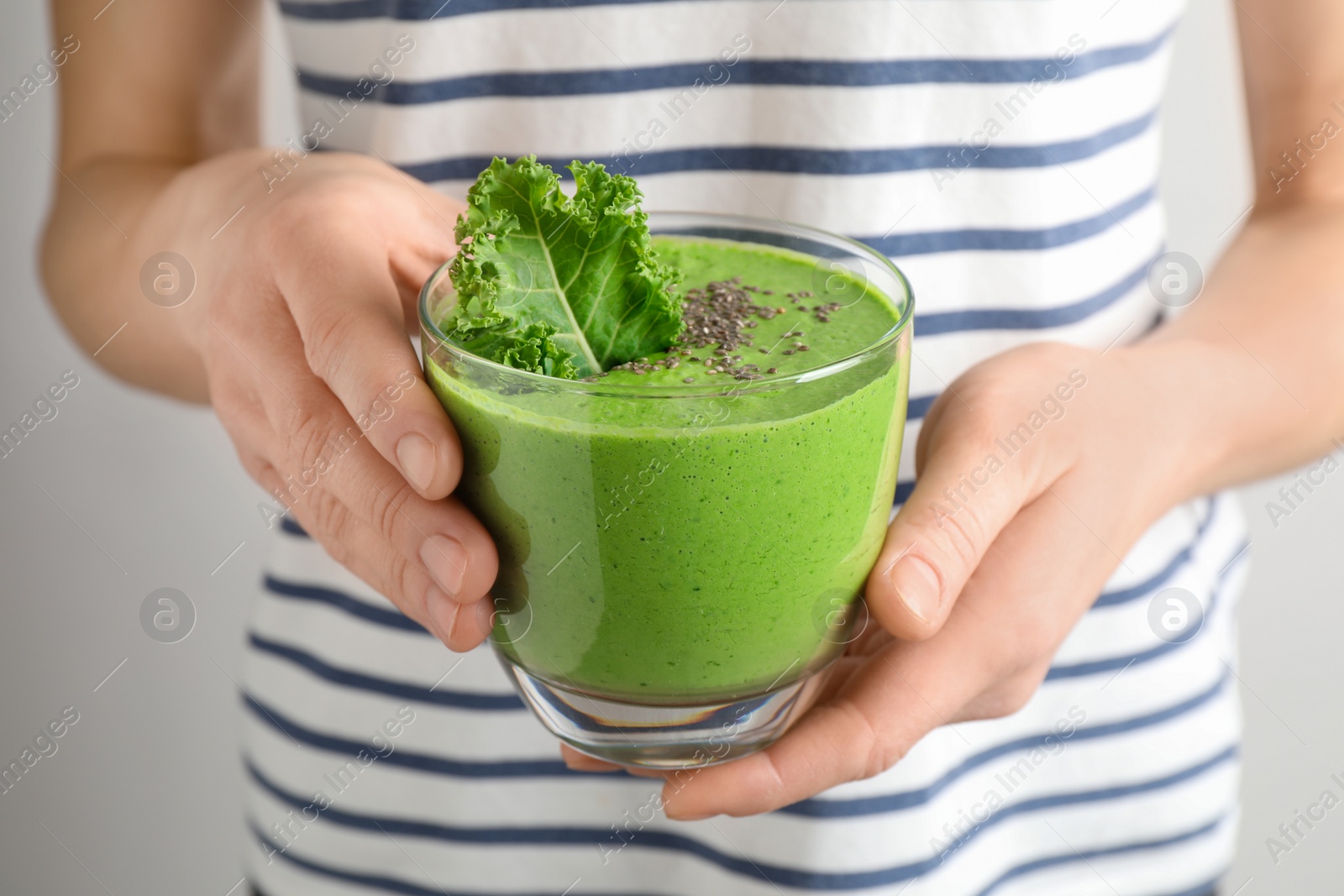 Photo of Woman holding tasty kale smoothie with chia seeds on light background, closeup