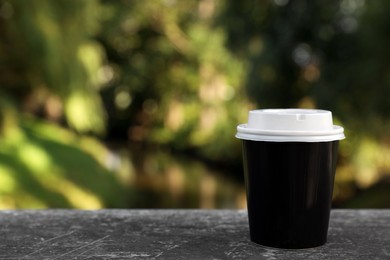 Photo of Takeaway paper cup with plastic lid on stone parapet outdoors, space for text