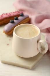 Photo of Cup of coffee and delicious eclairs covered with glaze on white wooden table