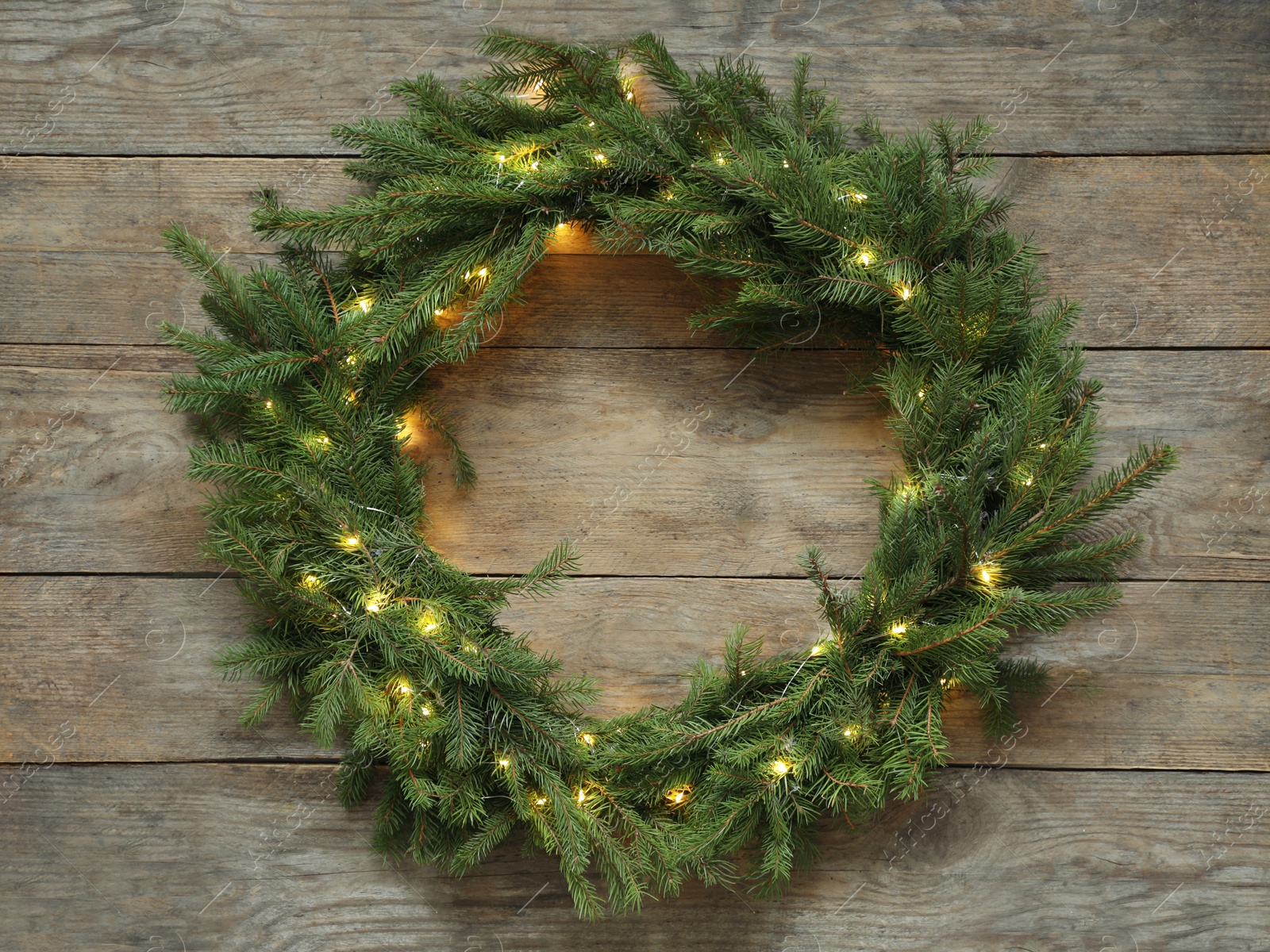 Photo of Beautiful Christmas wreath with festive lights on wooden background, top view