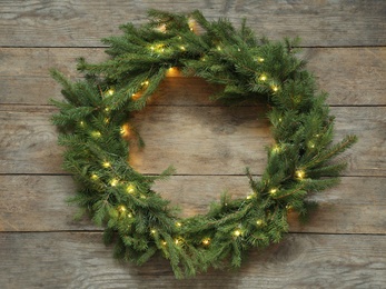 Photo of Beautiful Christmas wreath with festive lights on wooden background, top view