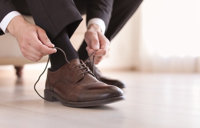 Photo of Man putting on elegant leather shoes indoors, closeup