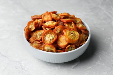 Bowl with cut dried kumquat fruits on white marble table, closeup