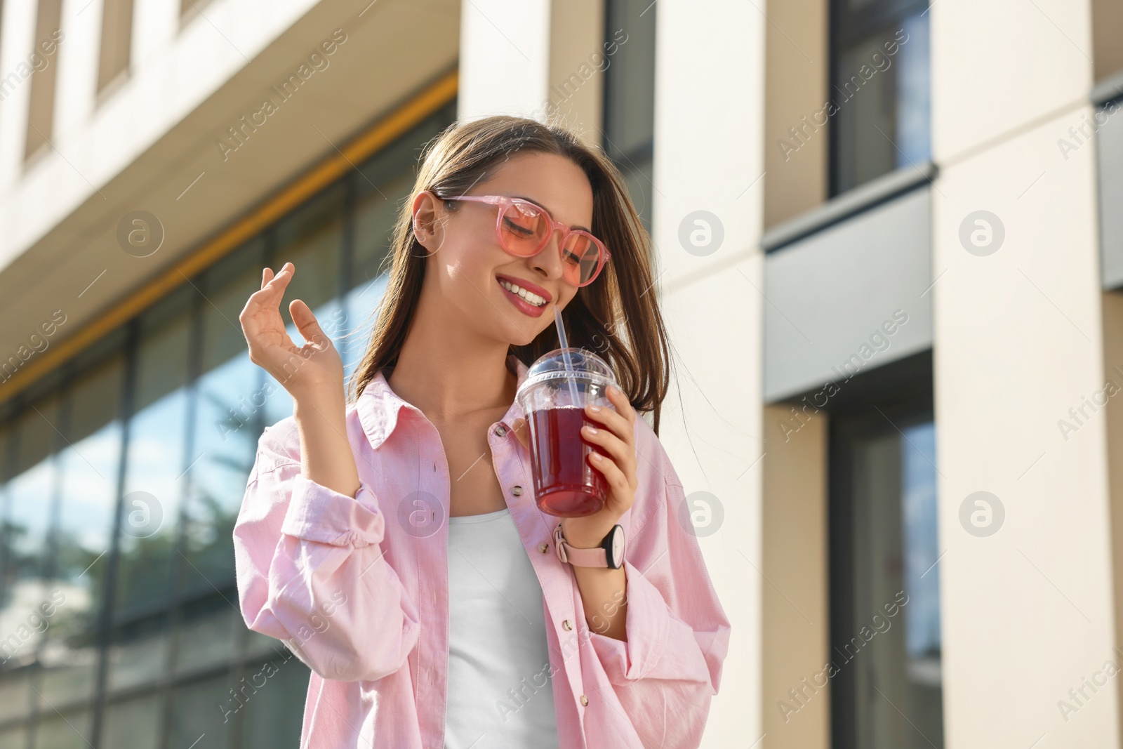 Photo of Young woman in sunglasses with plastic cup of fresh juice outdoors, space for text