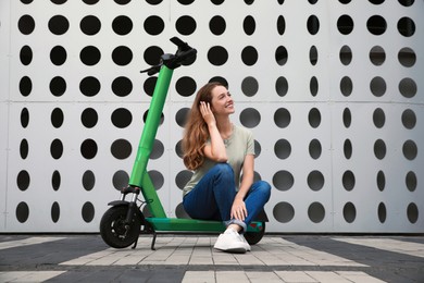 Photo of Happy woman sitting on modern electric kick scooter on city street