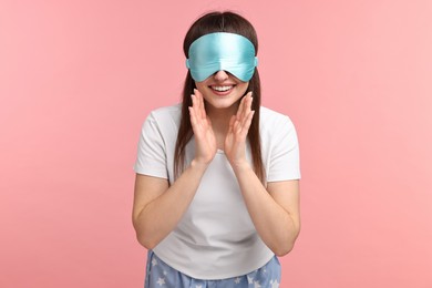 Happy woman in pyjama and sleep mask on pink background