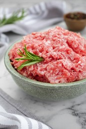 Photo of Bowl of raw fresh minced meat with rosemary on white marble table, closeup