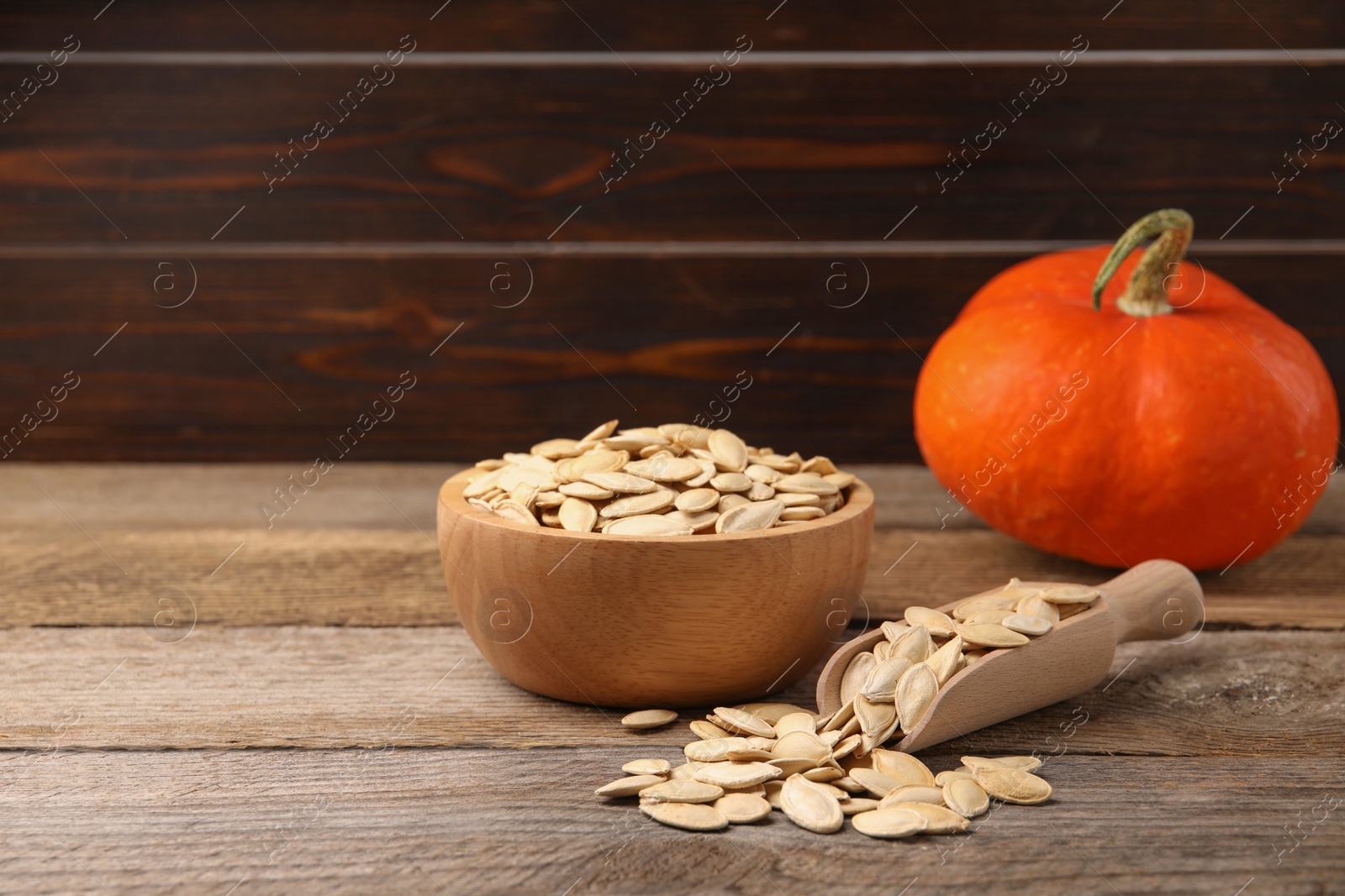 Bowl, scoop with seeds and fresh pumpkin on wooden table Photo of Bowl, scoop with seeds and fresh pumpkin on wooden table