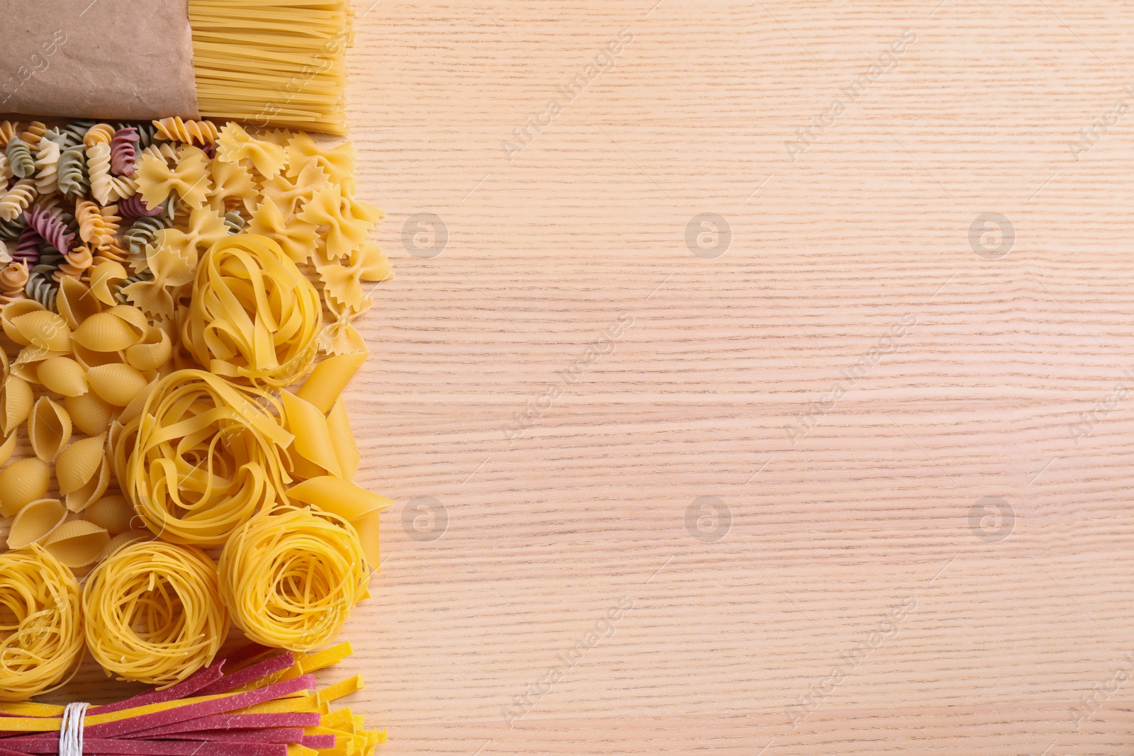 Photo of Different types of pasta on wooden table, flat lay. Space for text