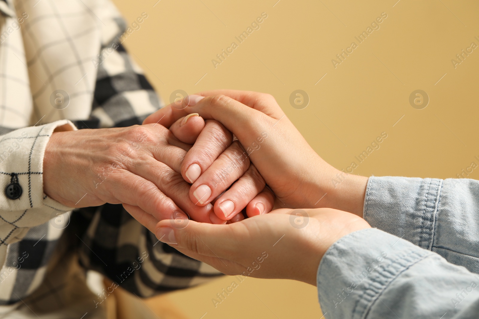 Photo of Young and elderly women holding hands on beige background, closeup