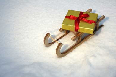 Wooden sleigh with gift box on snow outdoors. Space for text