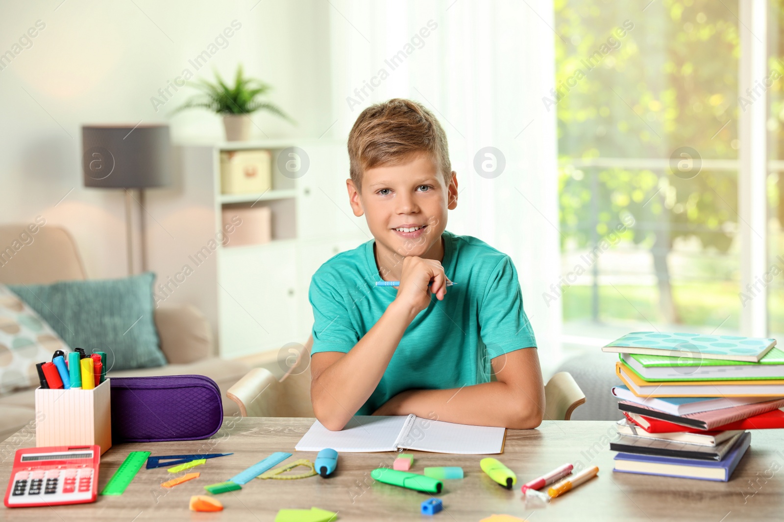 Photo of Cute boy doing homework at table with school stationery indoors