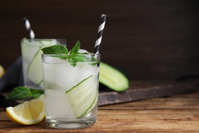 Glasses of refreshing cucumber water with mint on wooden table, space for text