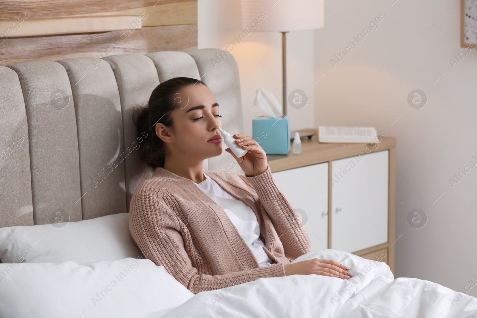 Photo of Sick young woman using nasal spray in bed at home