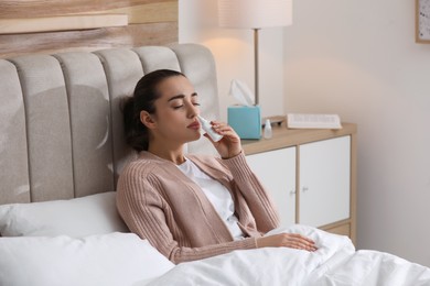 Sick young woman using nasal spray in bed at home